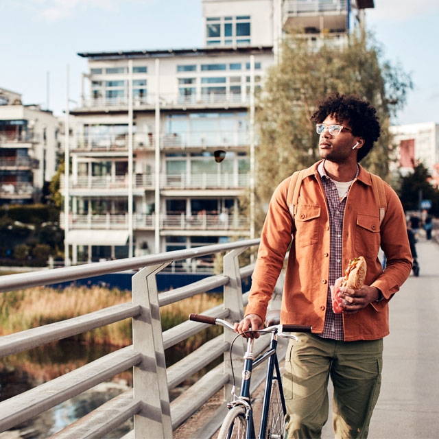 man som leder cykel över bro håller en baguette i handen